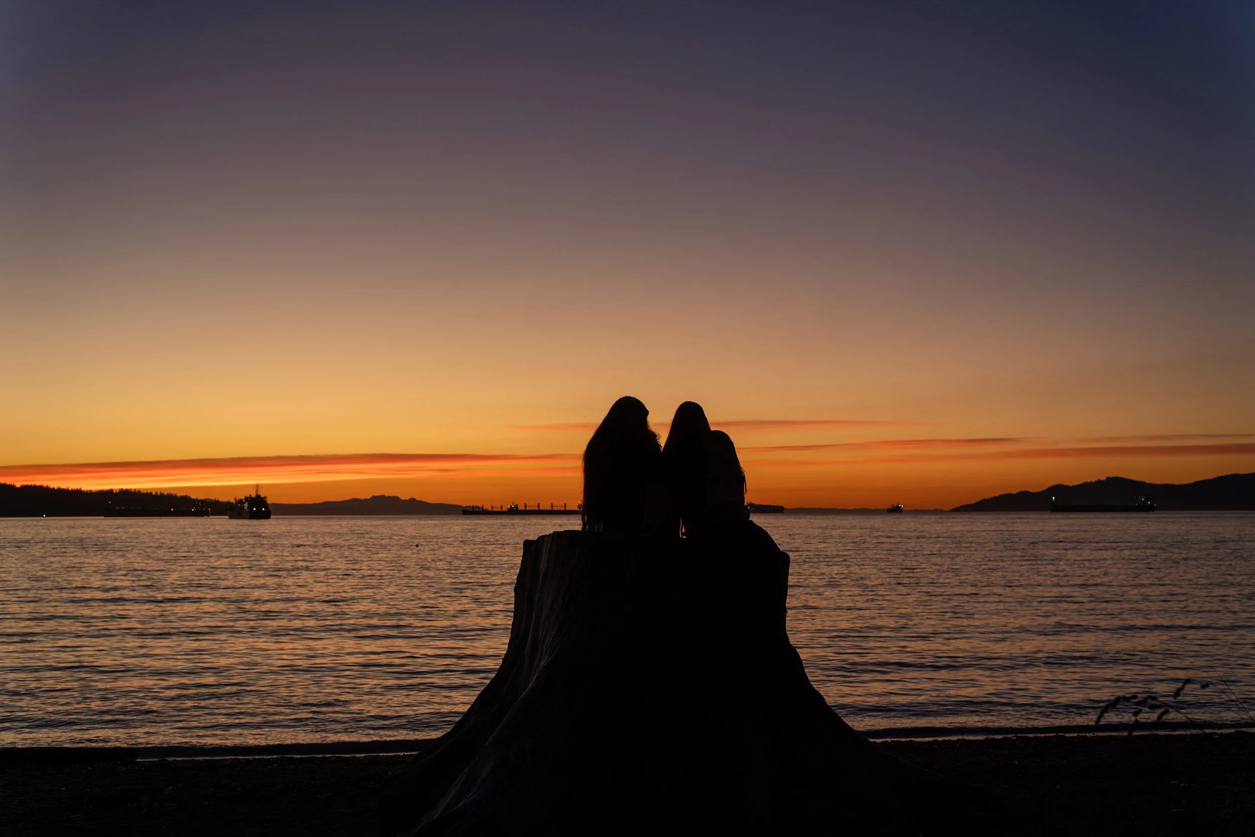 Friends sit on a tree stump at English Bay Beach at sunset, October 2026