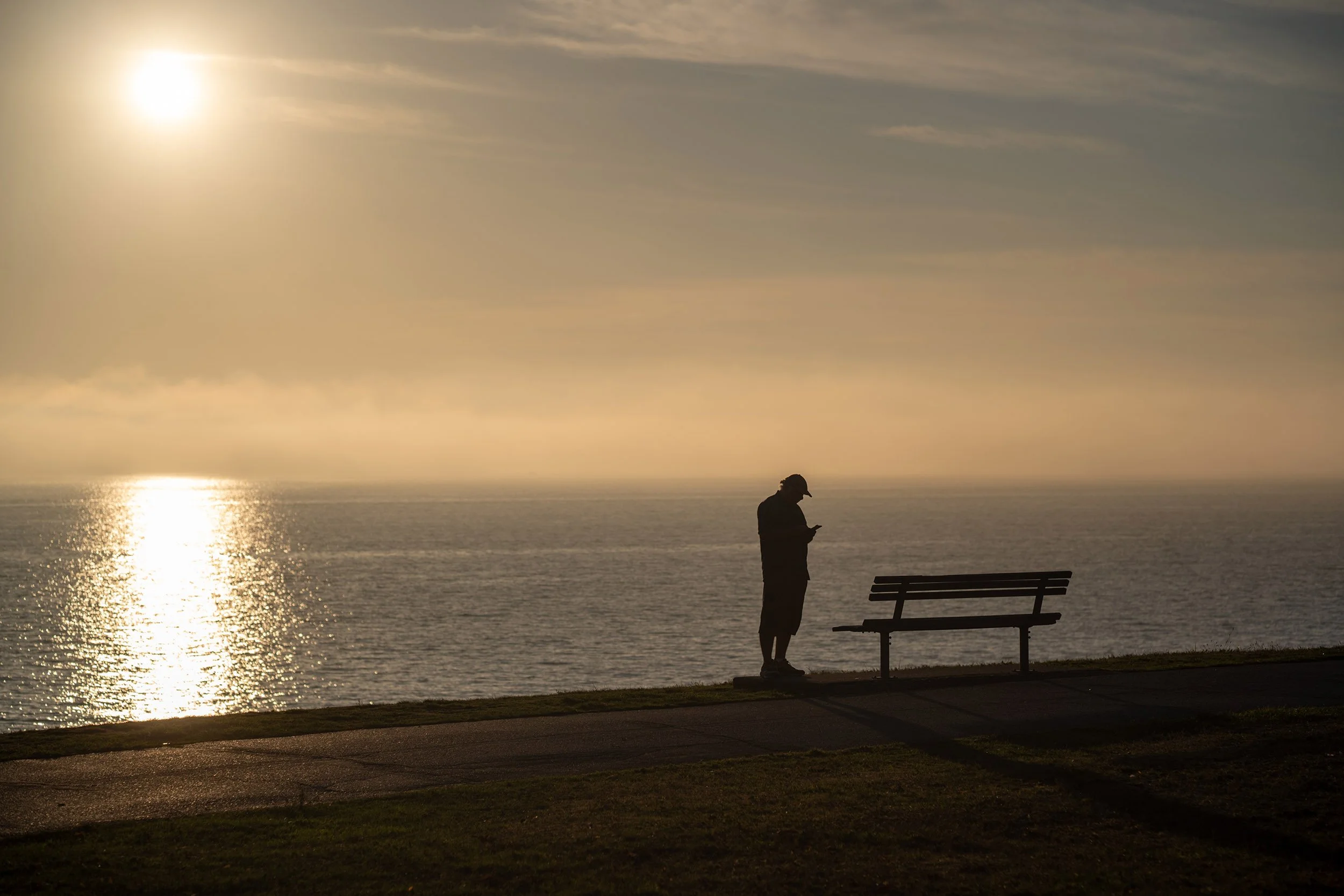 A man is on his phone during sunset at English Bay in Vancouver, October 2026