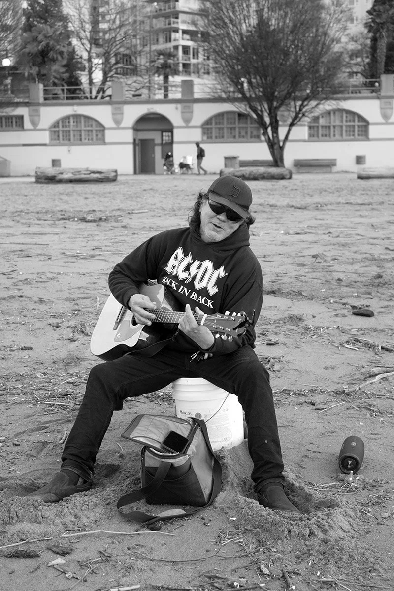 A man plays his guitar at English Bay Beach, December 2025