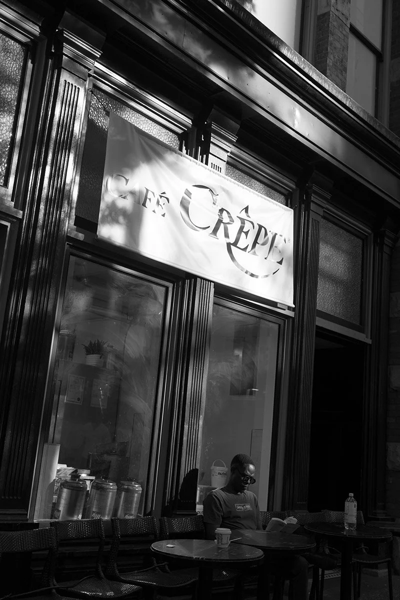 A man is reading a book at Café Crepe on Granville Street in Vancouver. Sample image from a Sony FE 40mm f/2.5 G and Sony A7 V.