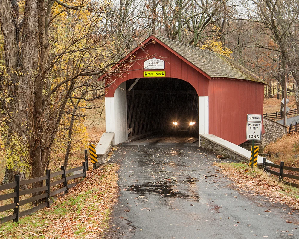 car emerges from covered bridge on rainy day