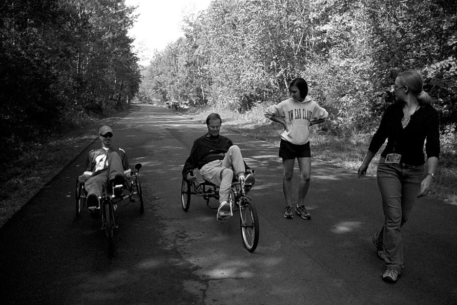 My dad and brother, Jimmy, ride recumbent bikes while my dad attends 'Aphasia Camp' held at a YMCA camp near New Auburn, Wis., as student and thearpist volunteers walk alongside. Put on by the University of Wisconsin-Eau Claire's communication sciences and disorders department, the camp is held annually and is organized to provide opportunities for people with aphasia to practice their communication skills and participate in meaningful activities in a supportive setting. September 2007.