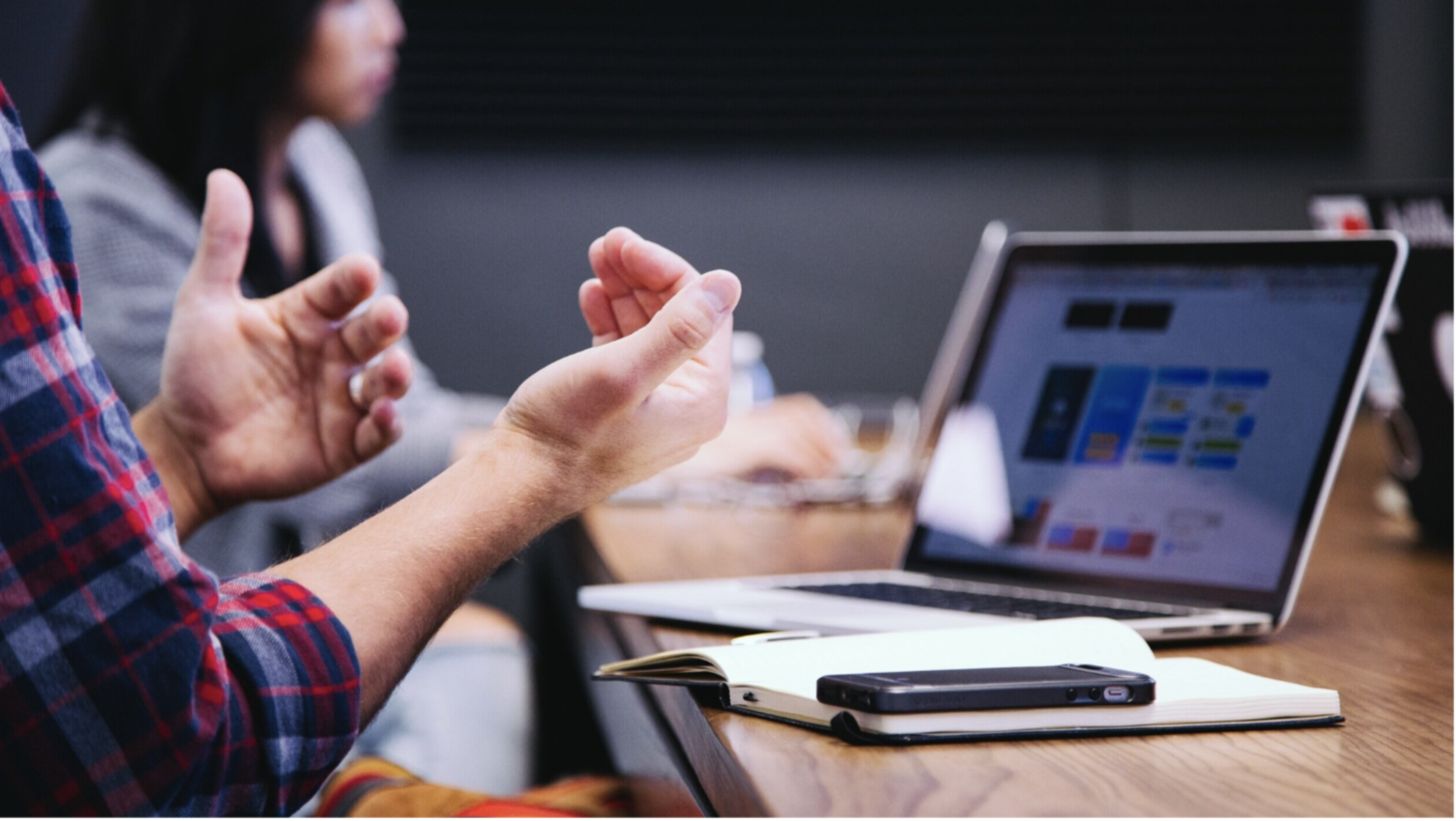 Pictuer of someones hands sitting at a desk with a laptop, notebook and mobile phone.png
