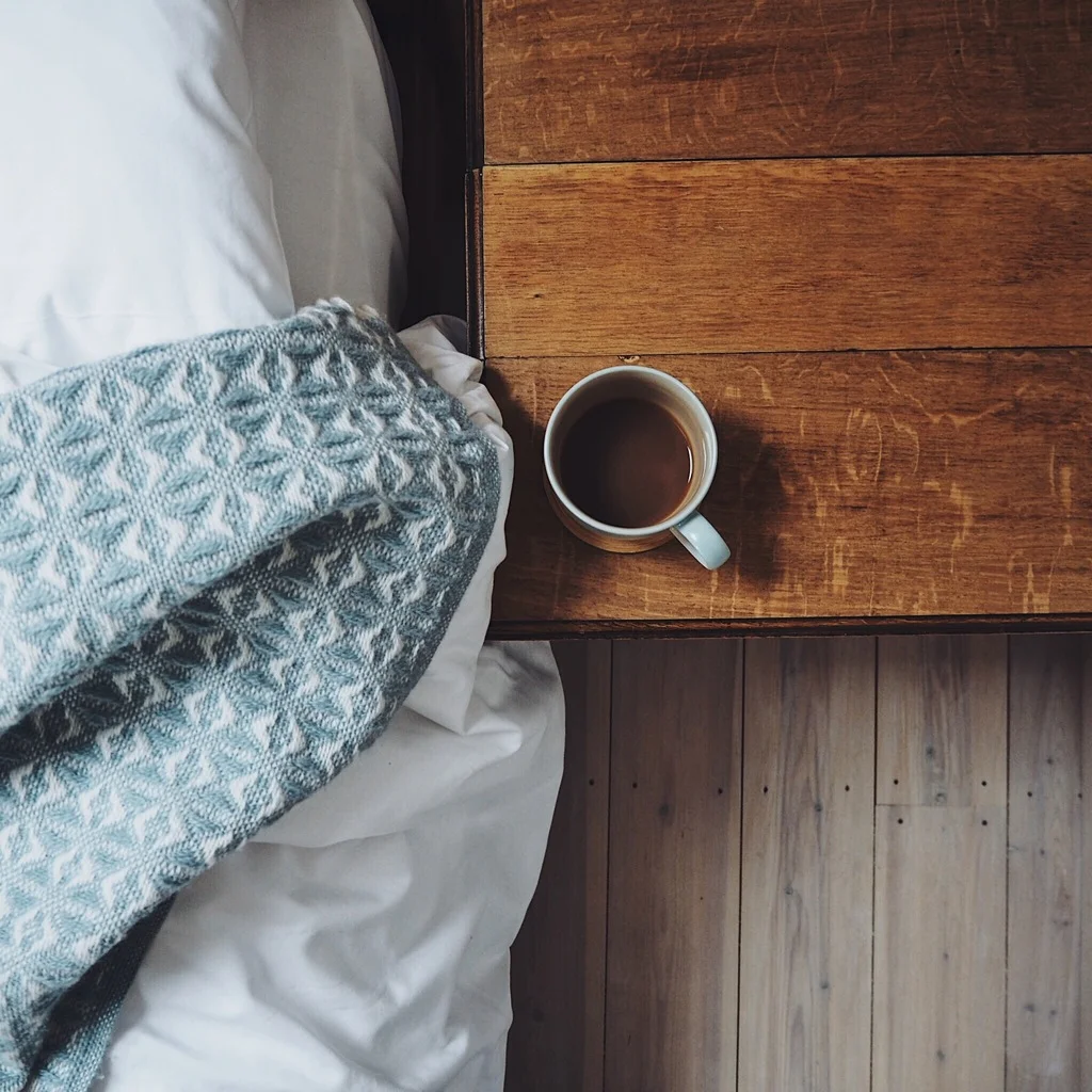 Cup of tea next to a bed with a blue blanket.jpg