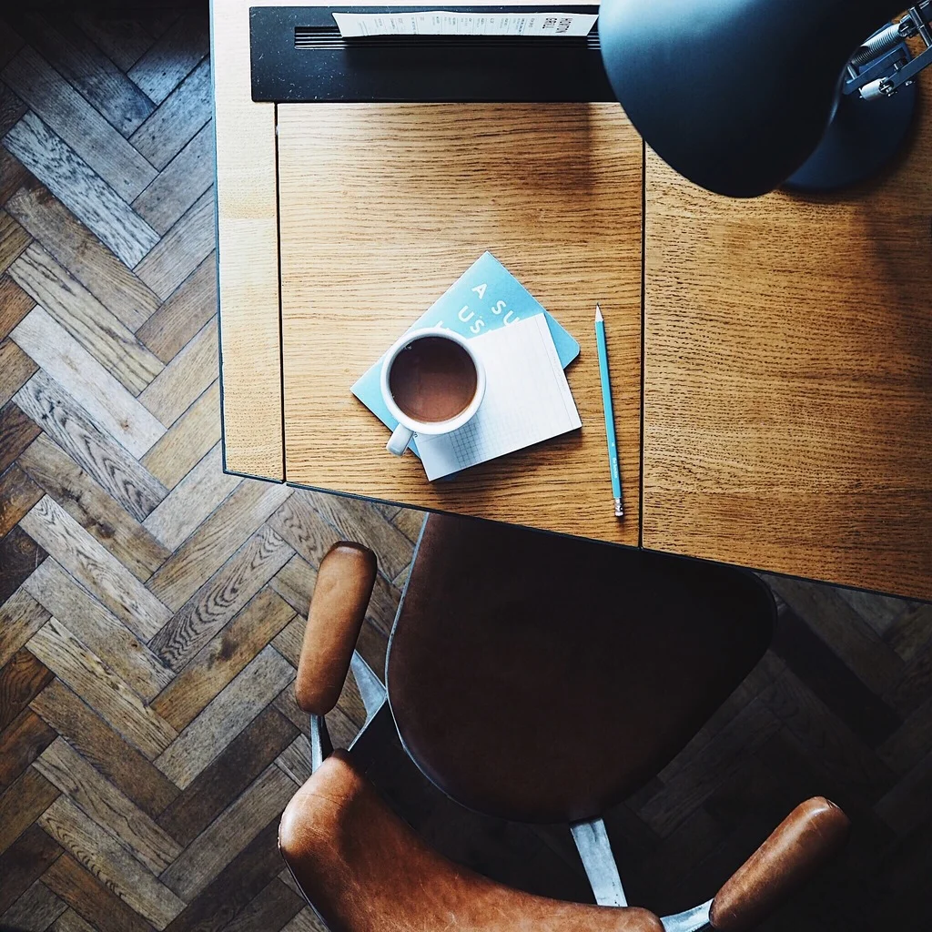 Cup of tea on a notebook on the corner of a mid-century desk with a leather chair.jpg