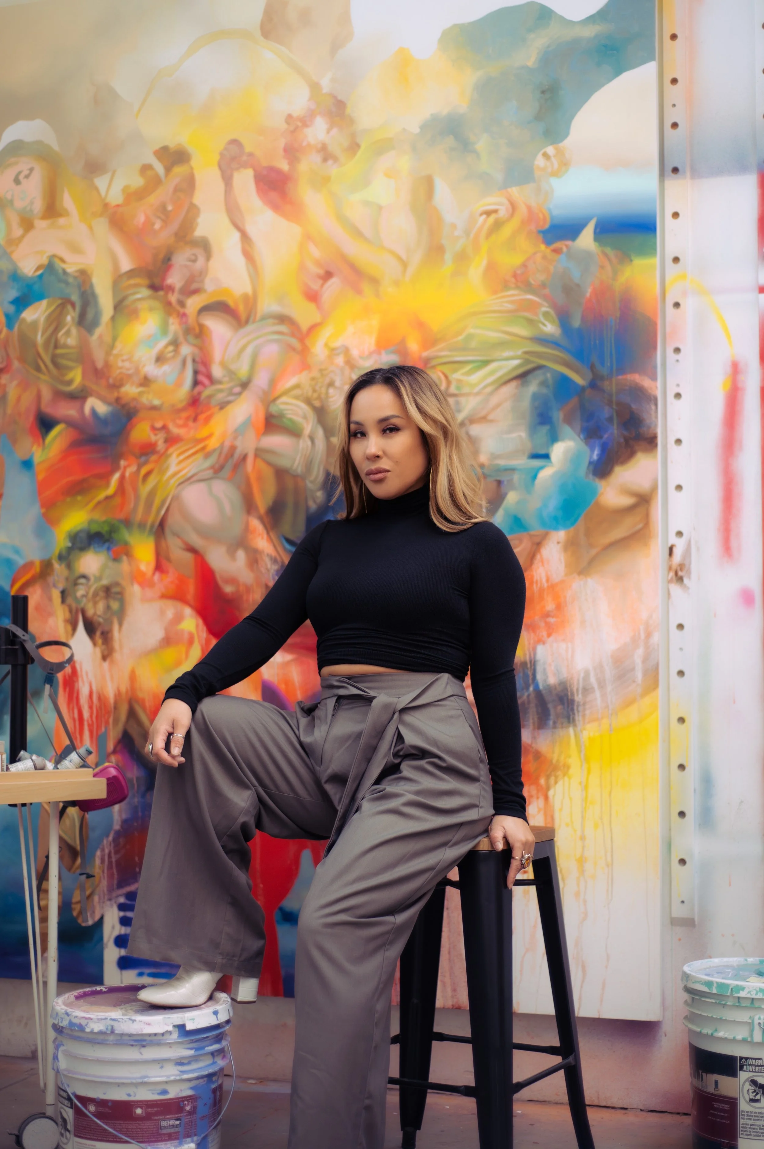  Portrait of the artist Allison Hueman sitting in front of her large abstract paintings 