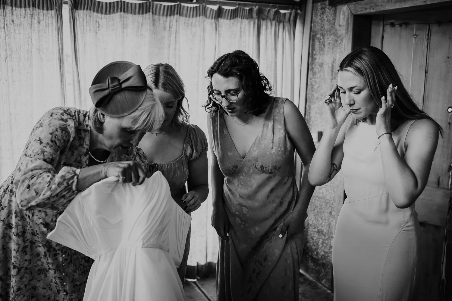 Mother of the bride and bridesmaids gathered around looking at a wedding dress, engaging in a discussion about the dress. Bridal Preparation Photo