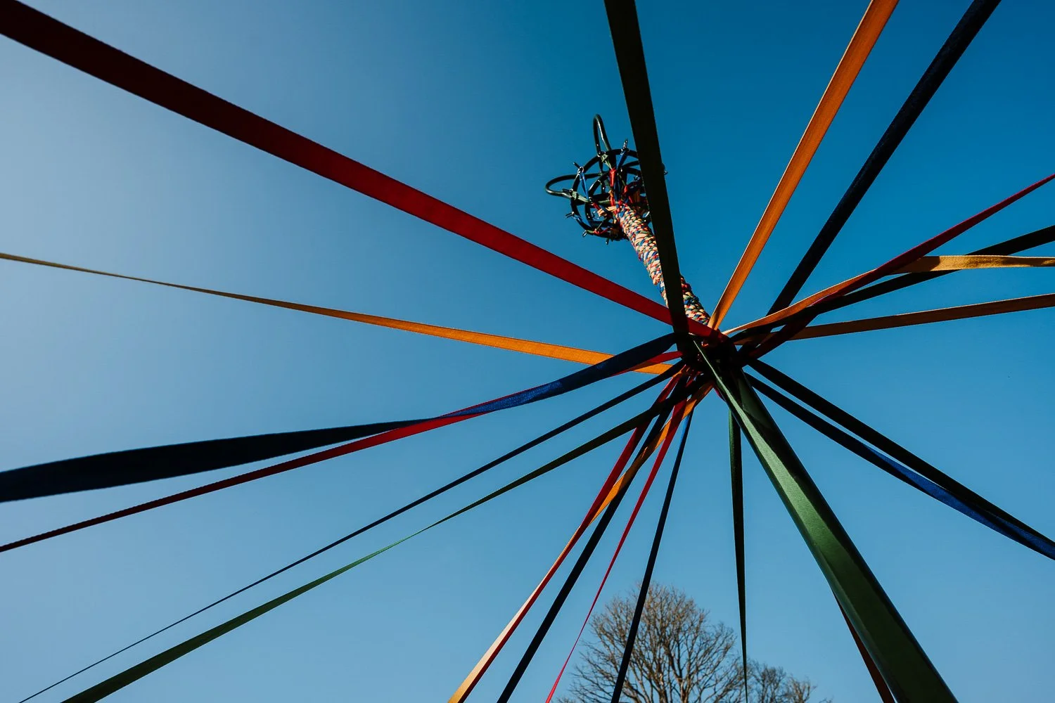 Looking up at a colorful ferris wheel with long spokes against a clear blue sky.