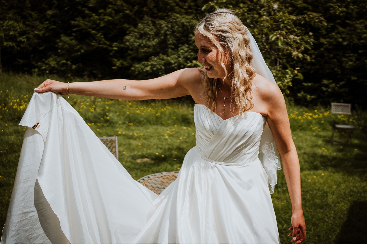 A reportage wedding photography moment, a bride lifting up her dirty dress smiling after she stepped into some chicken poo. 