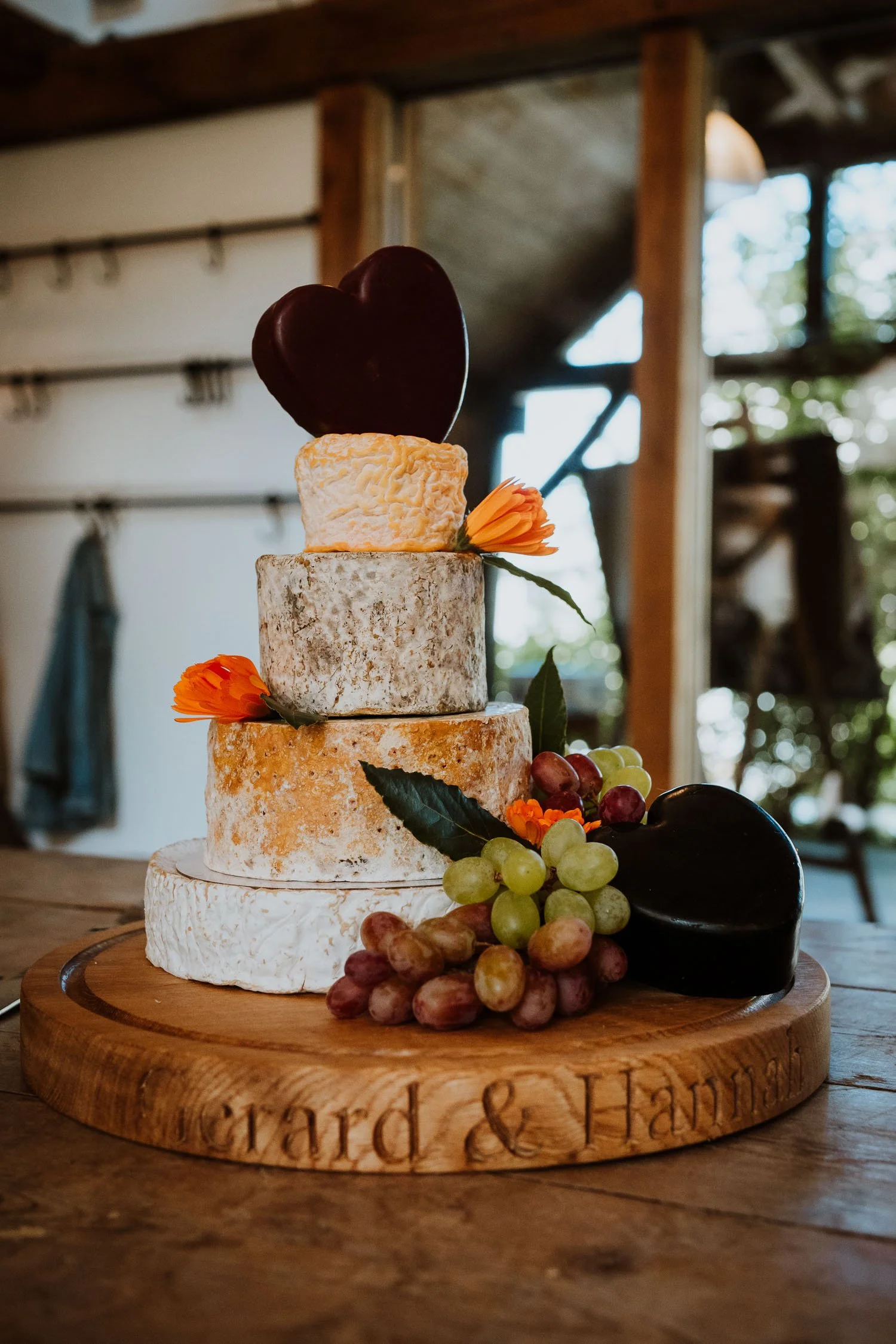 Cheese wheel with grapes and heart-shaped cheese, topped with a dark chocolate heart, on a wooden cheese board.