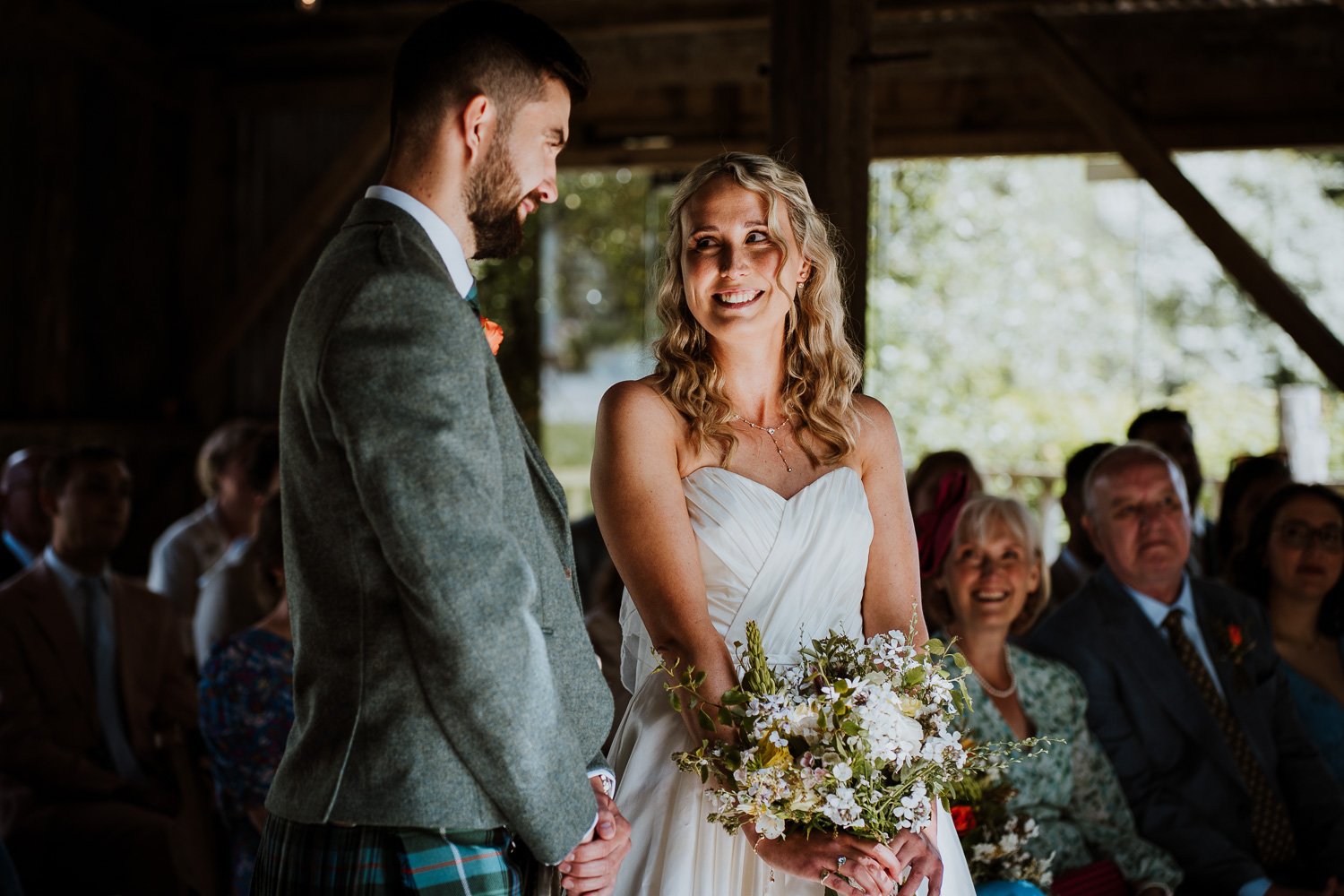 A bride and groom exchanging vows during a wedding ceremony indoors, with guests seated in the background.