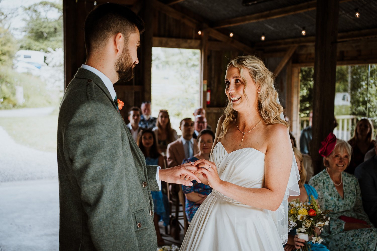 Bride and groom exchanging wedding vows inside a rustic barn with seated guests watching.