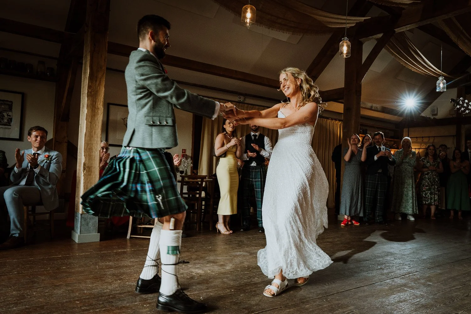 Bride and groom dancing at their wedding reception with guests clapping and smiling in the background.