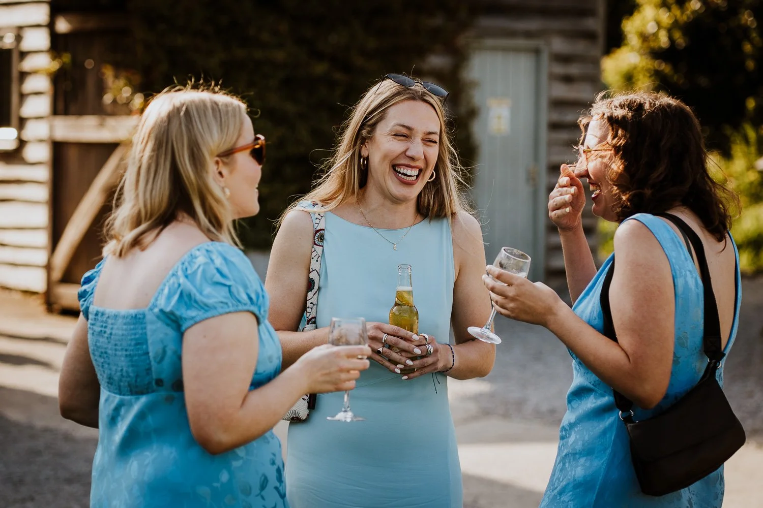 Bridesmaids laughing and talking outdoors, holding drinks, in a casual social setting.