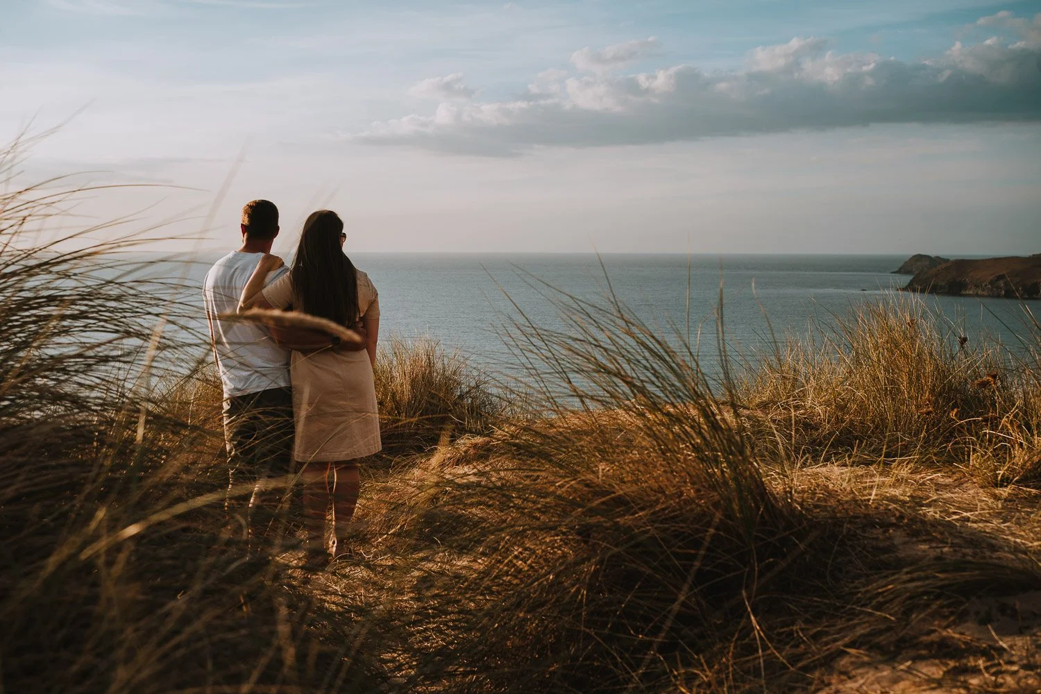A couple standing on a beach overlooking the ocean during sunset. Couple portrait taken during an engagement photo session