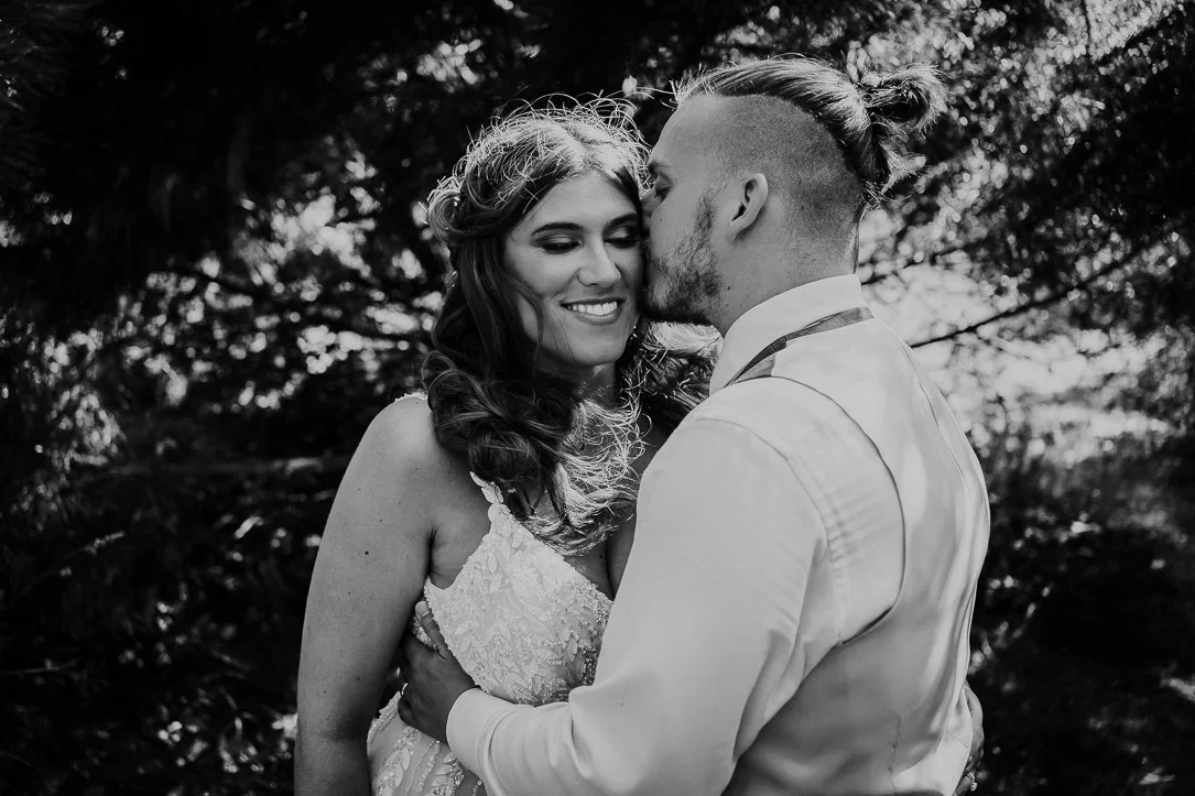 A happy couple on their wedding day, sharing a tender moment outdoors, with trees in the background. Natural Couple Portrait