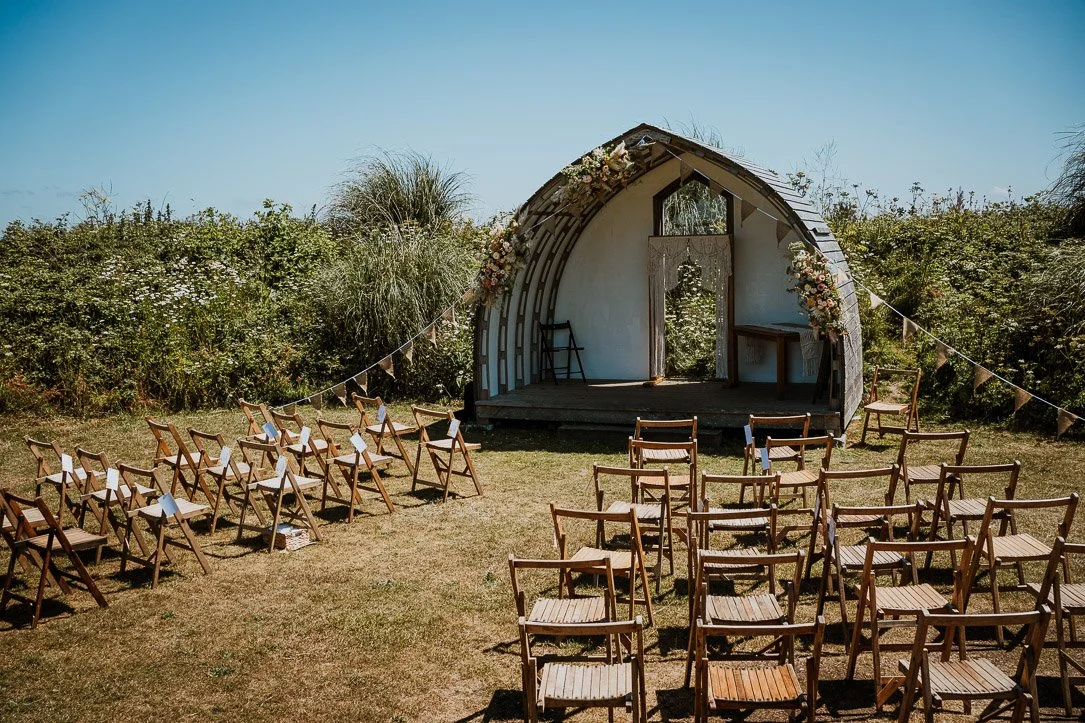 Outdoor wedding altar with chairs and floral decorations in a grassy field.
