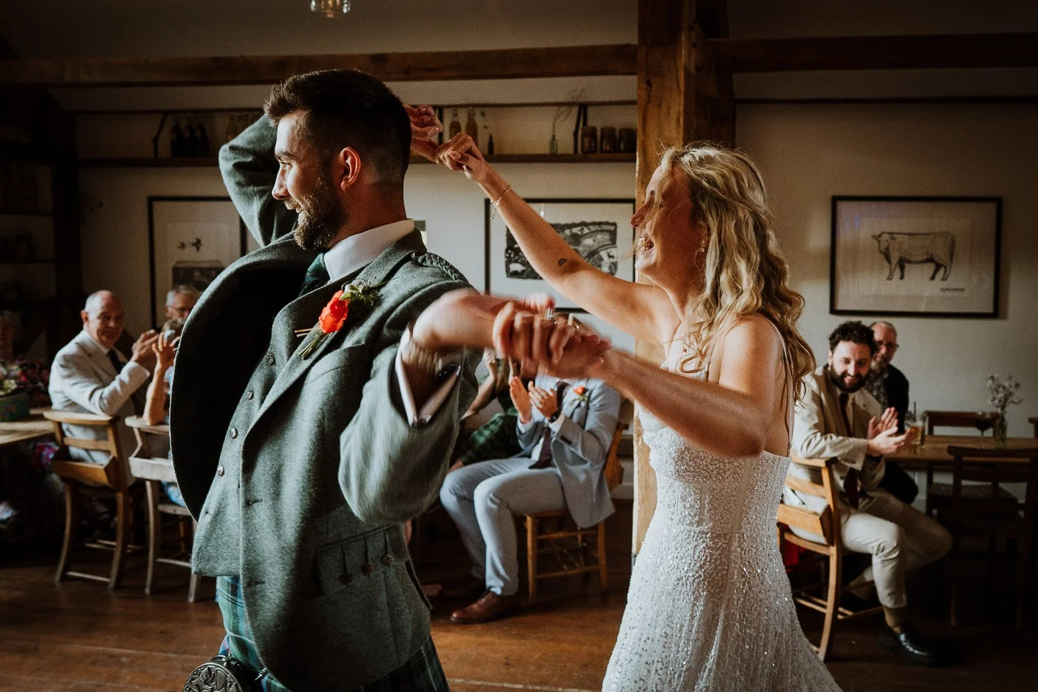 A bride and groom dancing at their wedding reception, with guests clapping and smiling in the background.