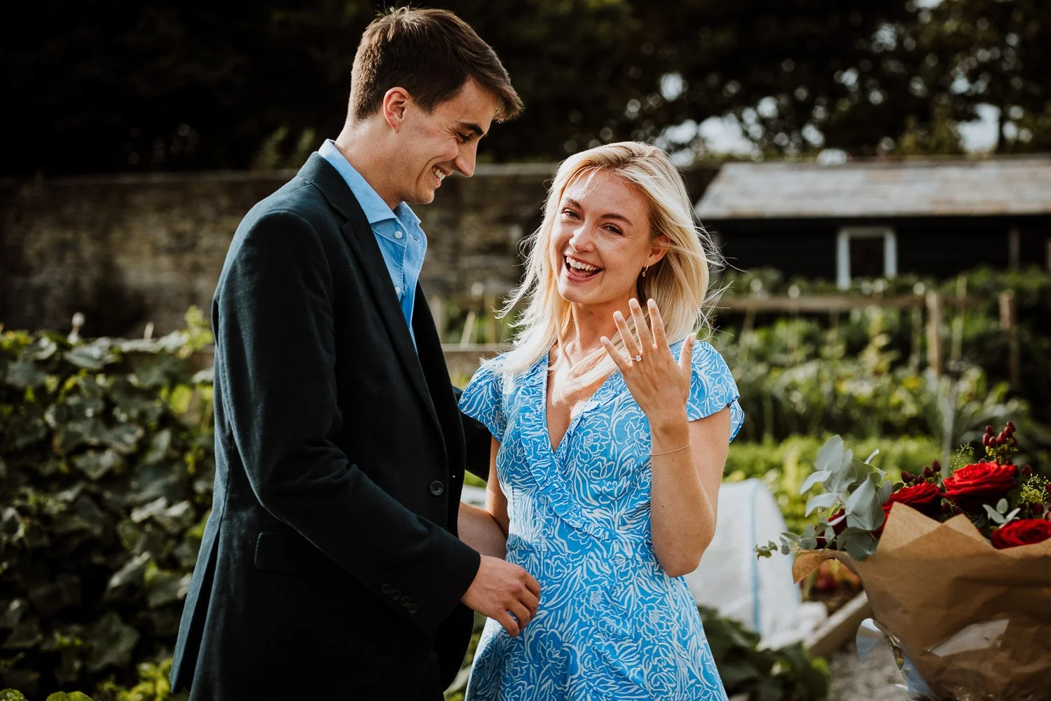 A man proposing marriage to a woman outdoors, with the woman smiling and showing her engagement ring. Natural Proposal Photography