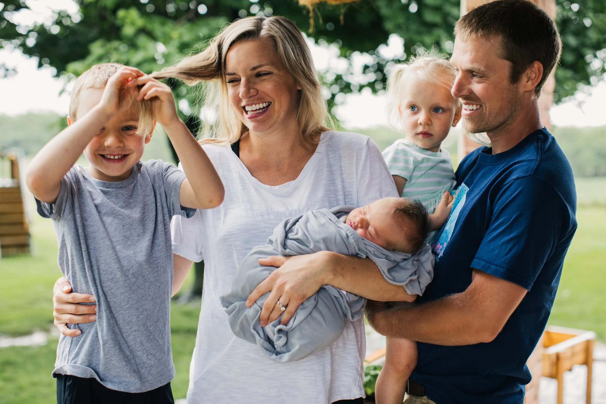 Family portrait of new born baby surrounded by family, laughing and smiling outside of their beautiful Maryland home.