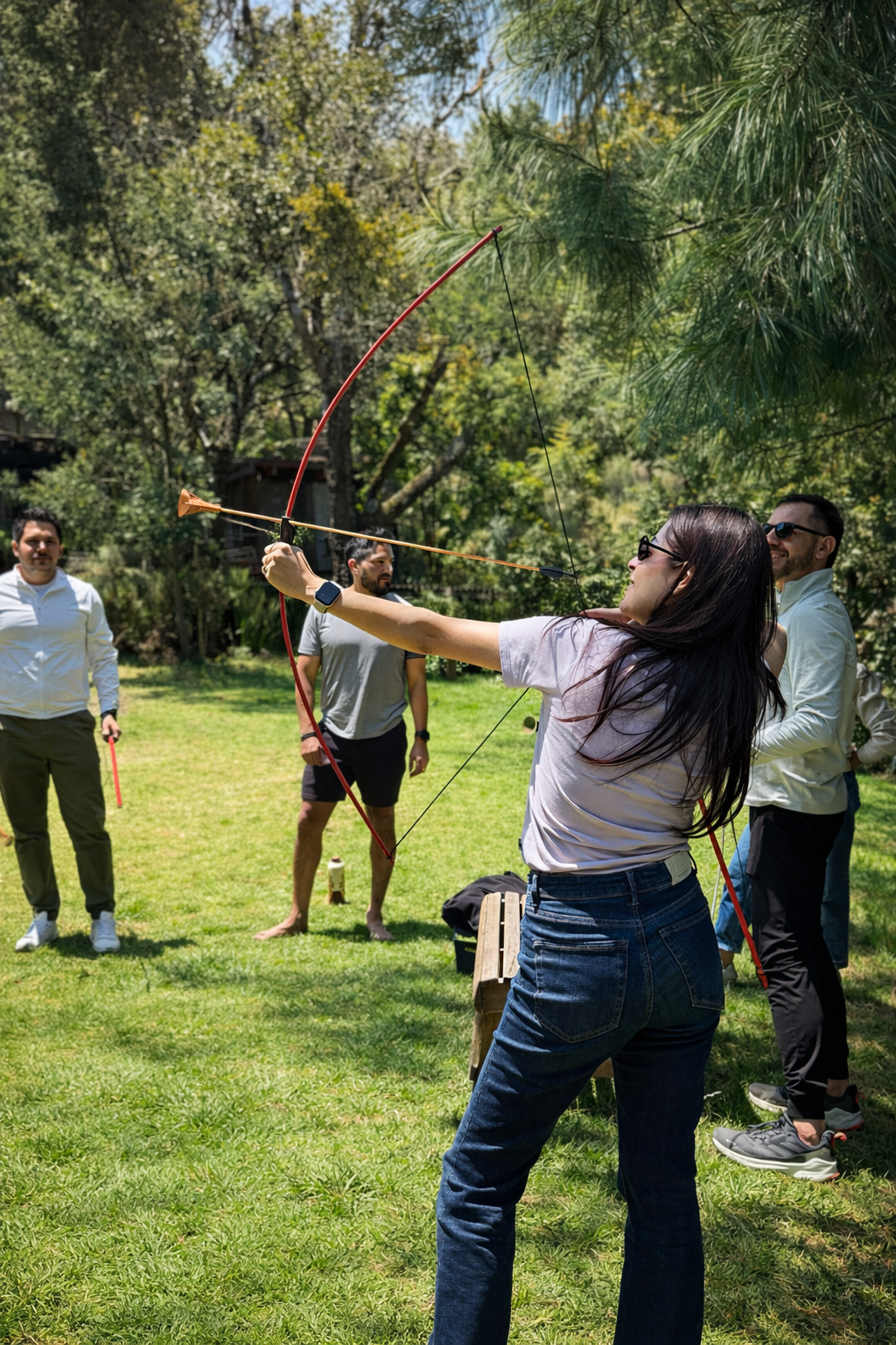 Niño practicando tiro con arco en un campo al aire libre, enfocando en la diana en el fondo.