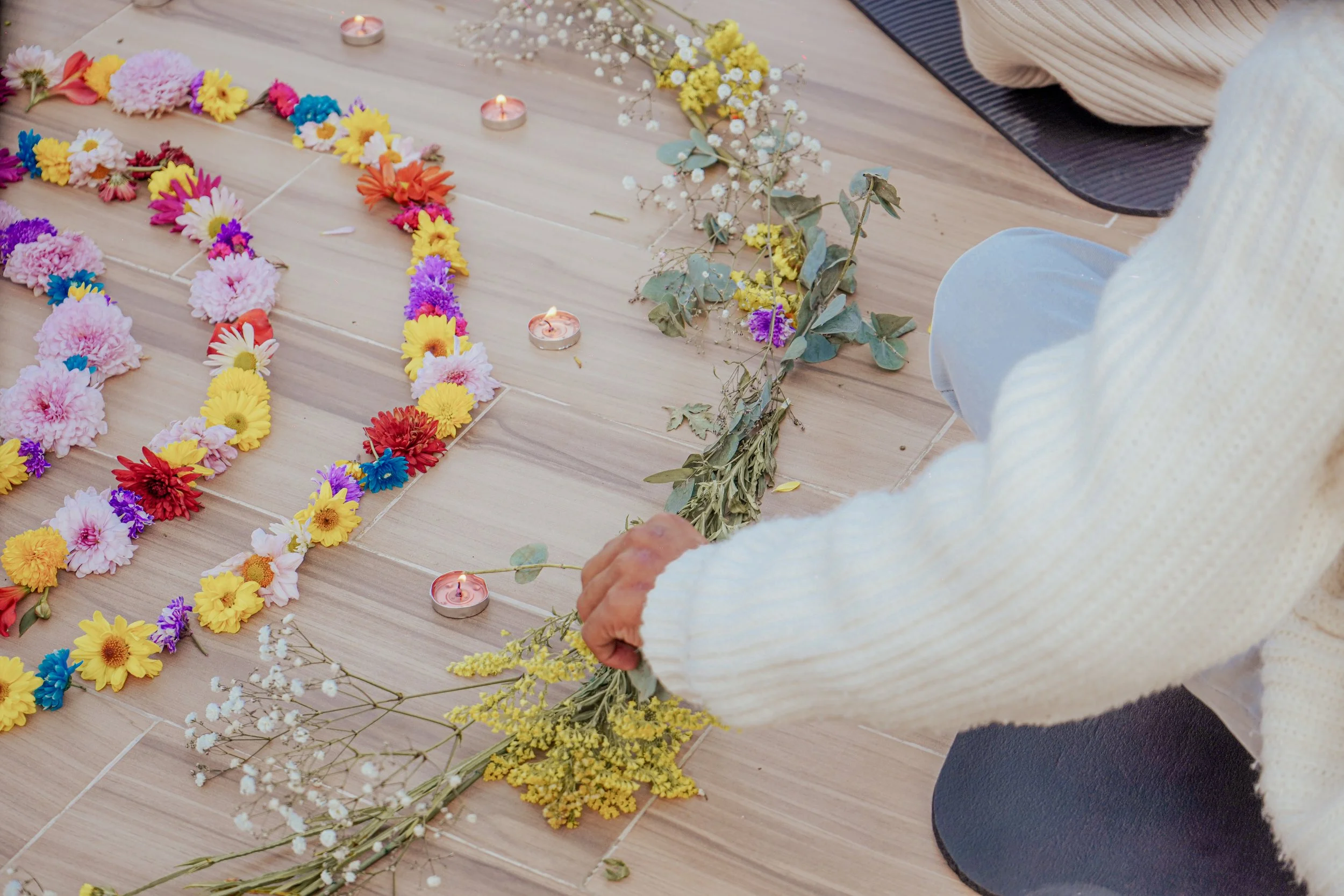 Persona arreglando flores y velas en el suelo con forma de corazón para ceremonia o ofrenda.