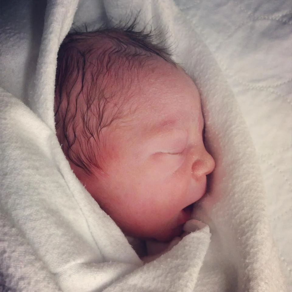 A newborn baby wrapped in white blanket, sleeping peacefully.