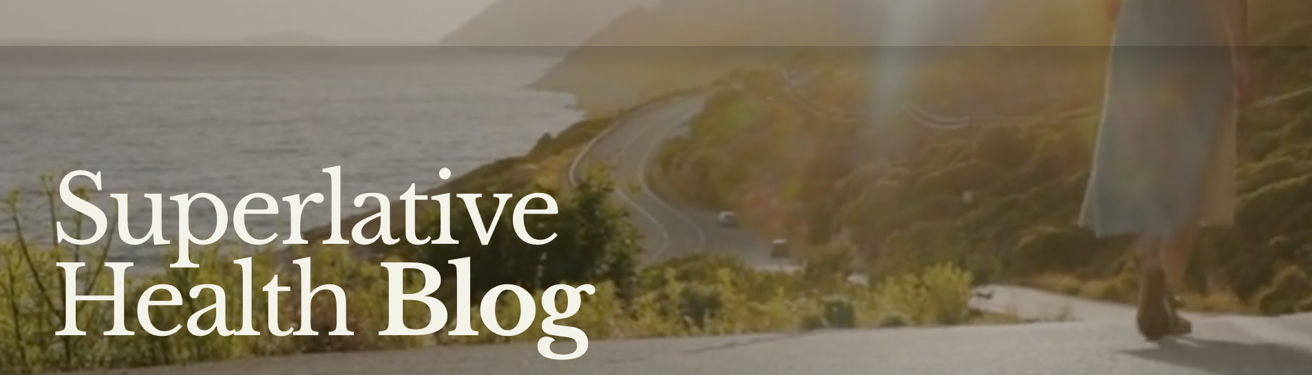 A person walking on a scenic mountain trail beside a body of water, with hills and a winding road in the background, overlaid with the text 'Superlative Health Blog'.