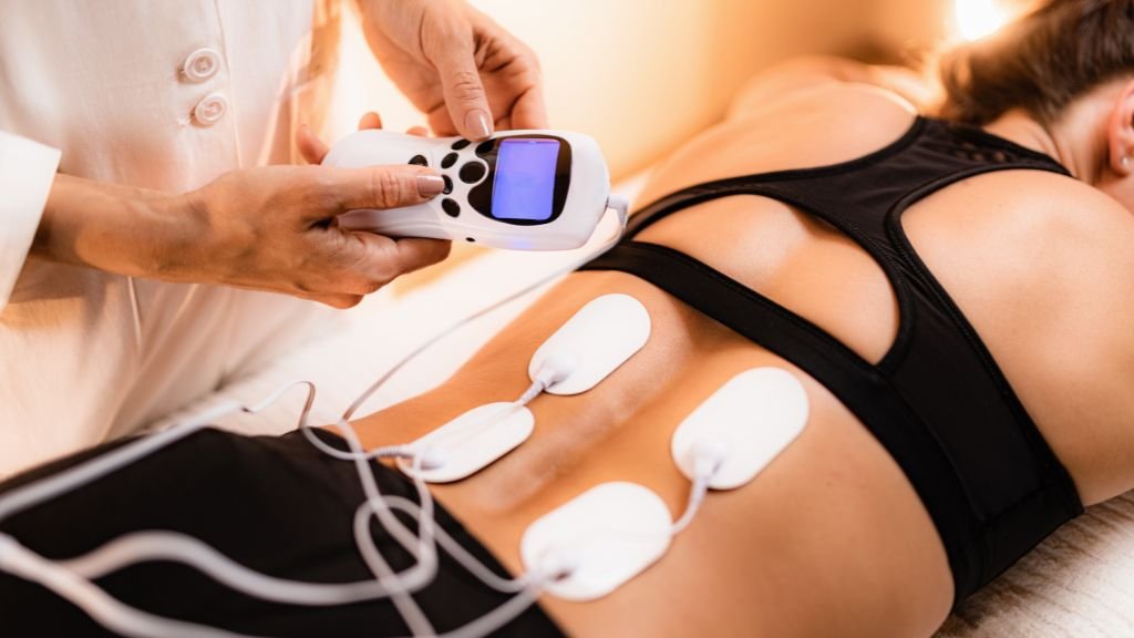 Medical professional using a device on a woman’s abdomen with four adhesive electrodes attached to her stomach.