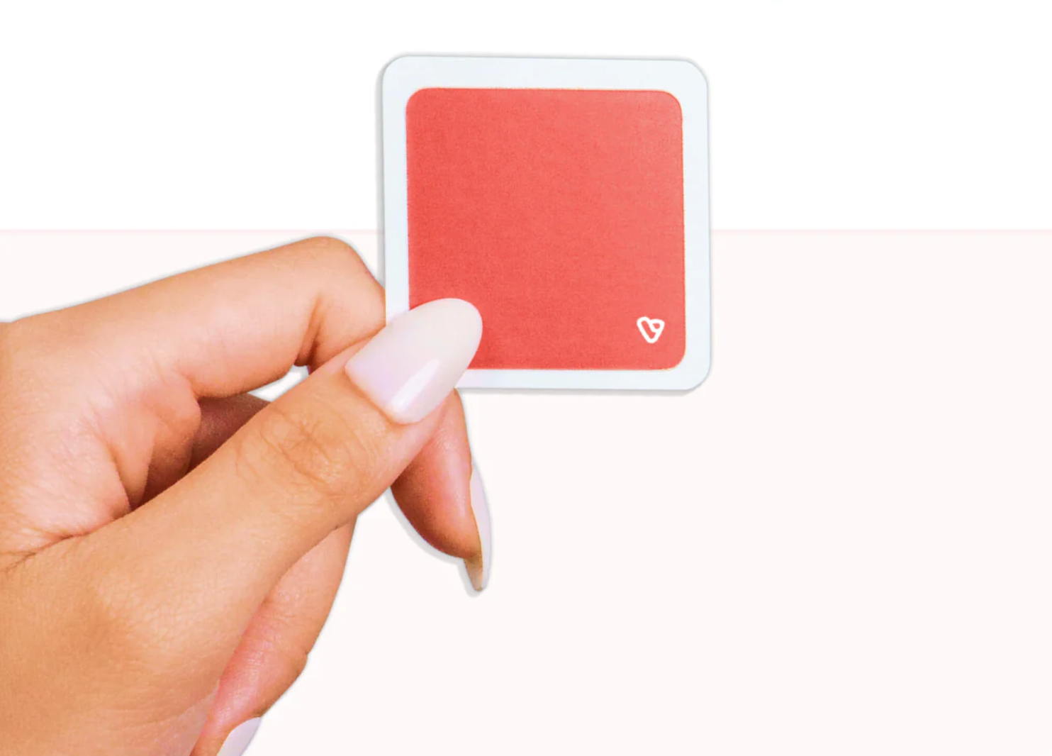A person's hand holding a small square card with a red background and a white heart icon in the lower right corner.