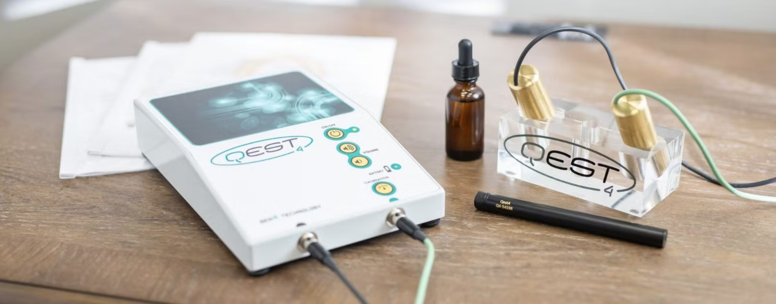 Medical testing equipment with a digital device labeled RE$T, test tubes, dropper, and wired probes on a wooden surface.