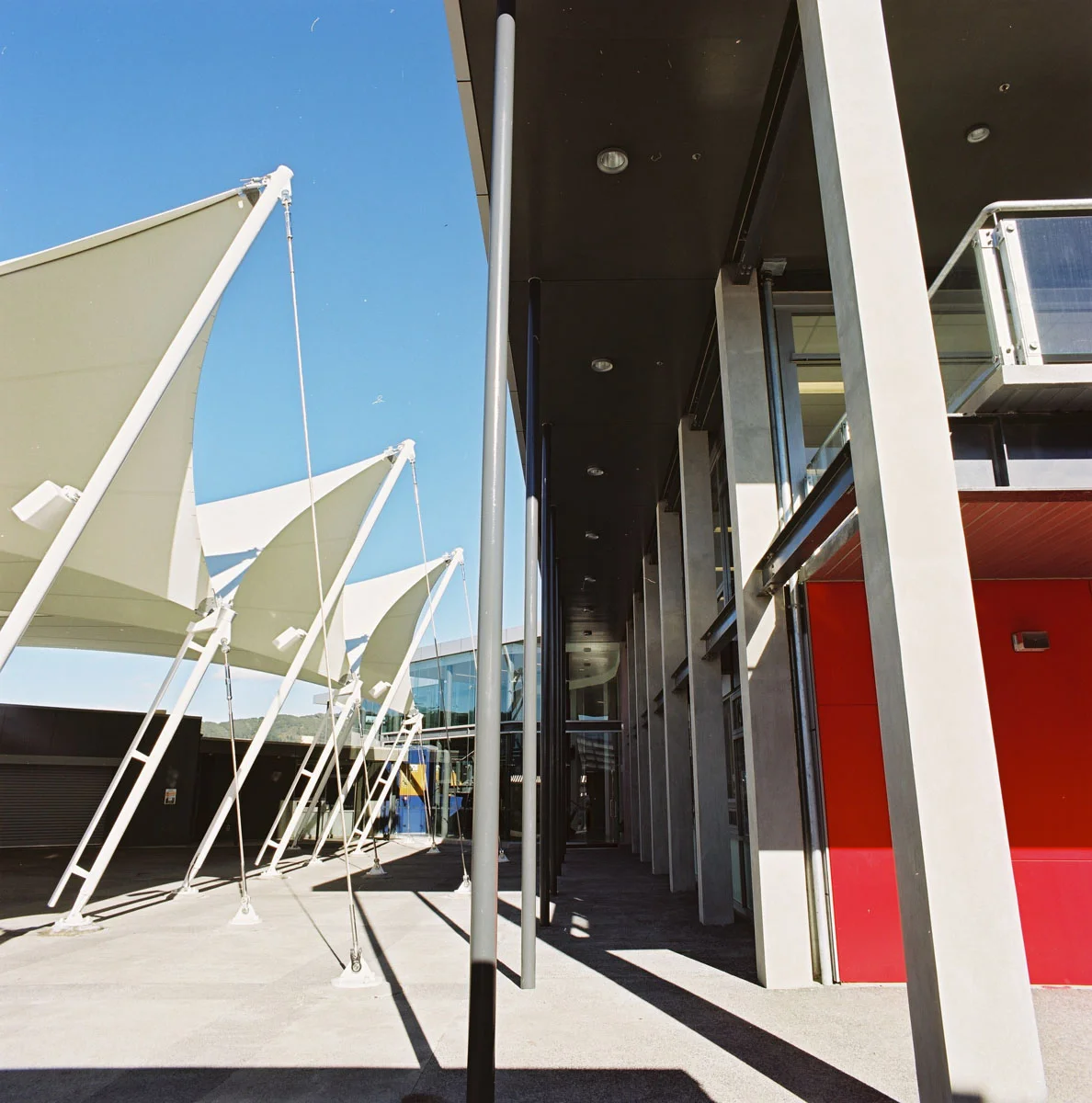 Located at the front entry heart of the campus, the design draws reference to the traditional school “cloistered edge” yet in a modern vernacular. A simple smooth steel skin plate punctuated centrally at the entry by a recessed curtain wall greets first time visitors. On the opposite side, a transparent edge engages the sheltered plaza. A double height transparent atrium linked at the upper level by a floating bridge structure, internally separates building structure and function. A sheltered multi purpose gathering space for students was an essential requirement of the brief. A Plaza was created and flanks the new Administration Building. A tensioned membrane canopy structure covers some 1,000sqm to create an indoor/outdoor space providing shelter from all weather conditions.