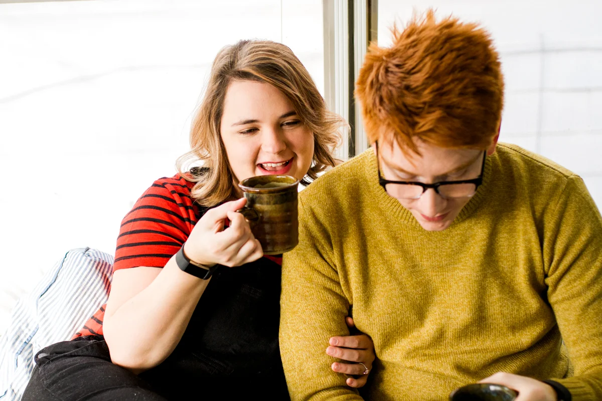 Laughing together in bed holding coffee during an intimate in-home couples session in Kansas City, MO