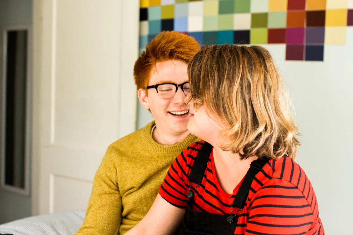 laughing together on a bed during a colorful in-home couples session in Kansas City, MO