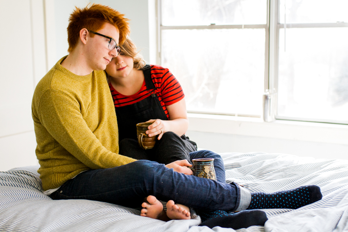  Cuddling together with coffee on a bed during an intimate in-home couples session in Kansas City, MO 