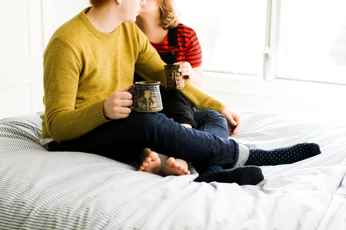 Cuddling together with coffee on a bed during an intimate in-home couples session in Kansas City, MO