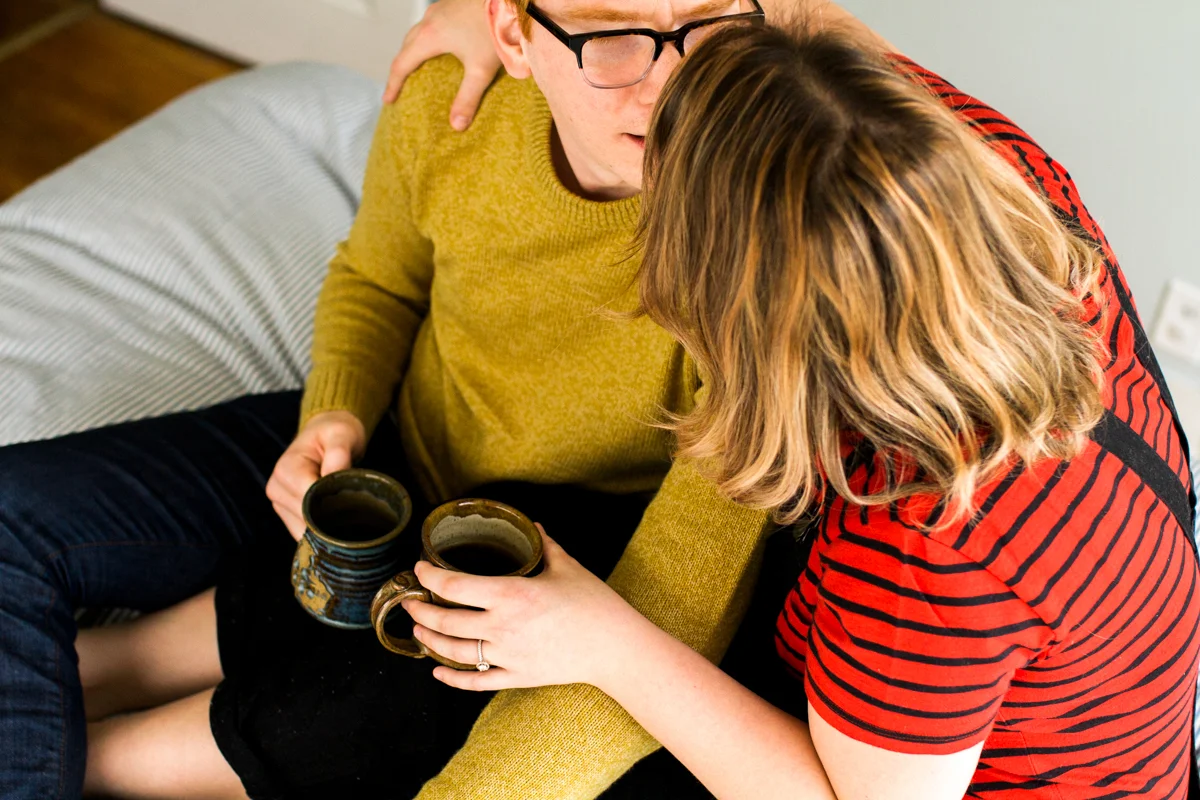 cuddling close with coffee on a bed during an intimate in-home couples session in Kansas City, MO