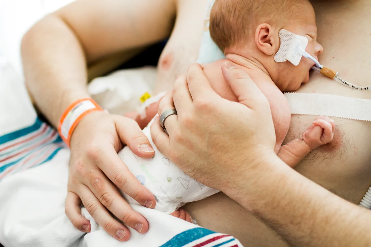 Rebecca Clair Photography lifestyle NICU newborn photography Children's Mercy Hospital father doing skin to skin with his baby father's hands on baby