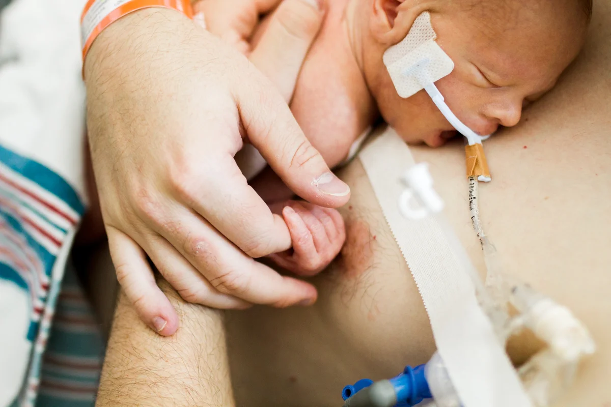 Rebecca Clair Photography lifestyle NICU newborn photography Children's Mercy Hospital father doing skin to skin with his baby father holding baby's hand