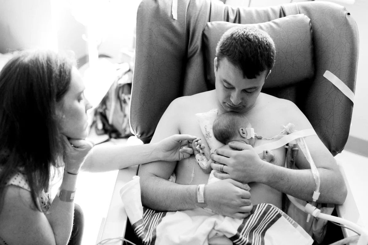 Rebecca Clair Photography lifestyle NICU newborn photography Children's Mercy Hospital father doing skin to skin with his baby mother holding baby's hand black and white photo