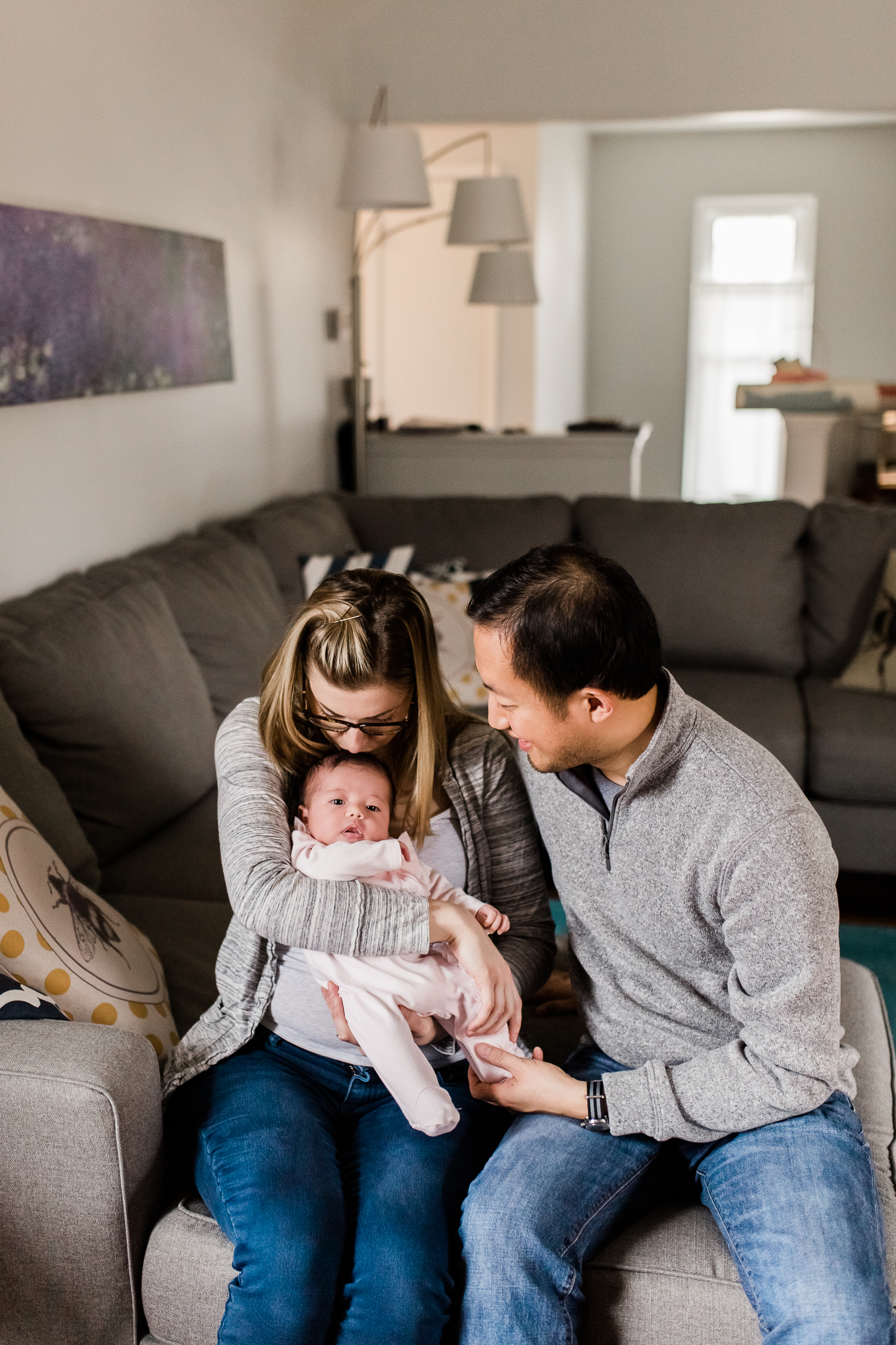  couple holding their newborn baby in the living room, mother kissing her newborn baby's head, Kansas City lifestyle newborn photographer, in-home newborn session 