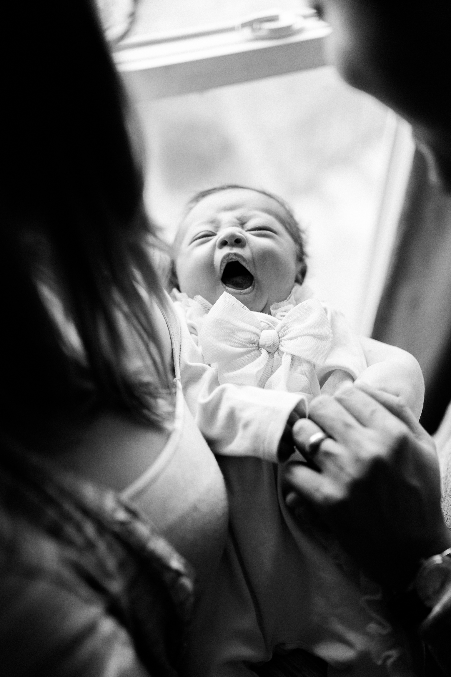  black and white portrait of a couple holding their newborn baby by a window, yawning newborn baby, Kansas City lifestyle newborn photographer, in-home newborn session 