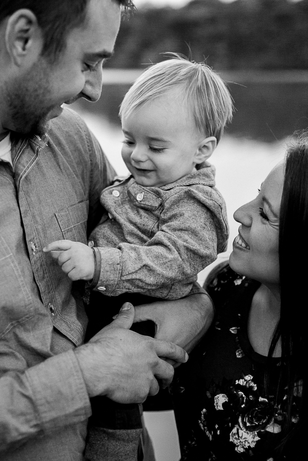  Black and white portrait of parents cuddling their son by the lake, Kansas City lifestyle photographer, sunrise family session at Shawnee Mission Park, Rebecca Clair Photography 