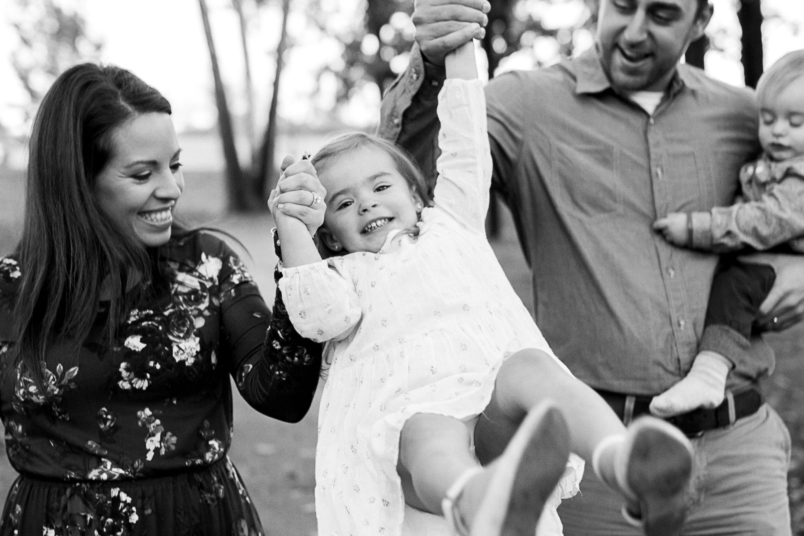  Black and white candid photo of family swinging daughter at the park, Kansas City lifestyle photographer, Shawnee Mission Park, Rebecca Clair Photography 