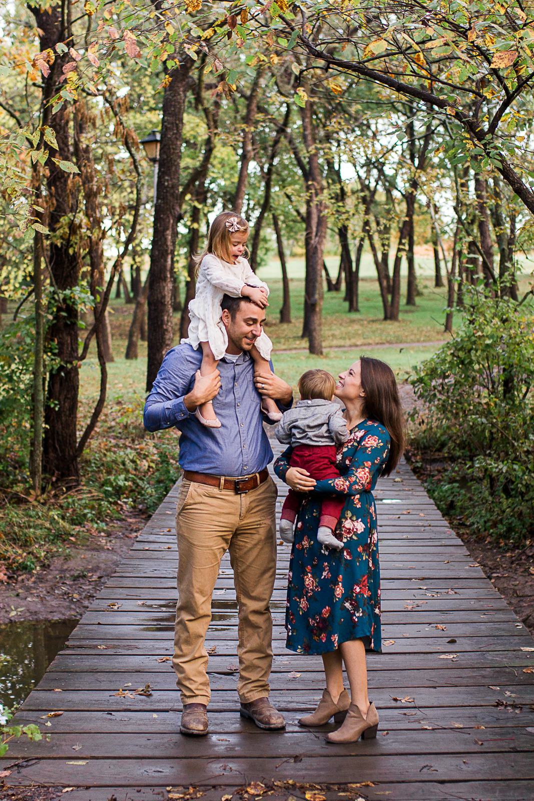  Daughter sits on dads shoulders and family stands in the woods, fall family photos, Shawnee Mission Park sunrise session, Rebecca Clair Photography 
