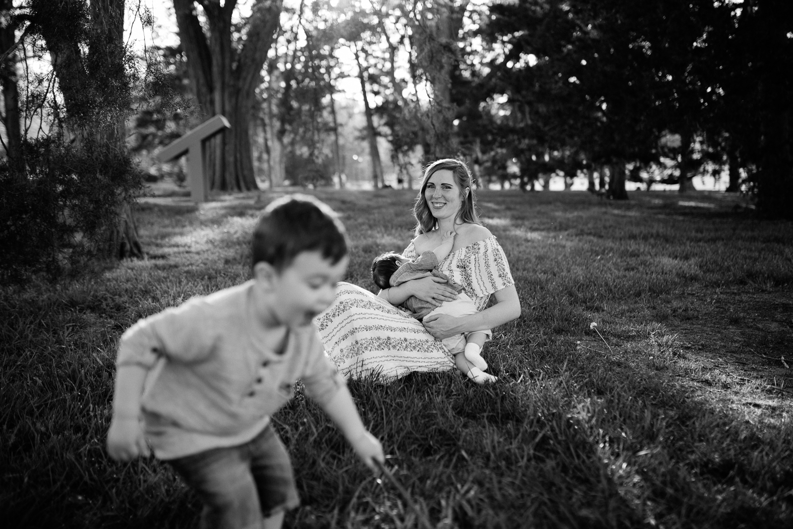  Black and white portrait of mother breastfeeding her baby while her toddler plays nearby, Kansas City breastfeeding session, lifestyle family photographer, Rebecca Clair Photography 