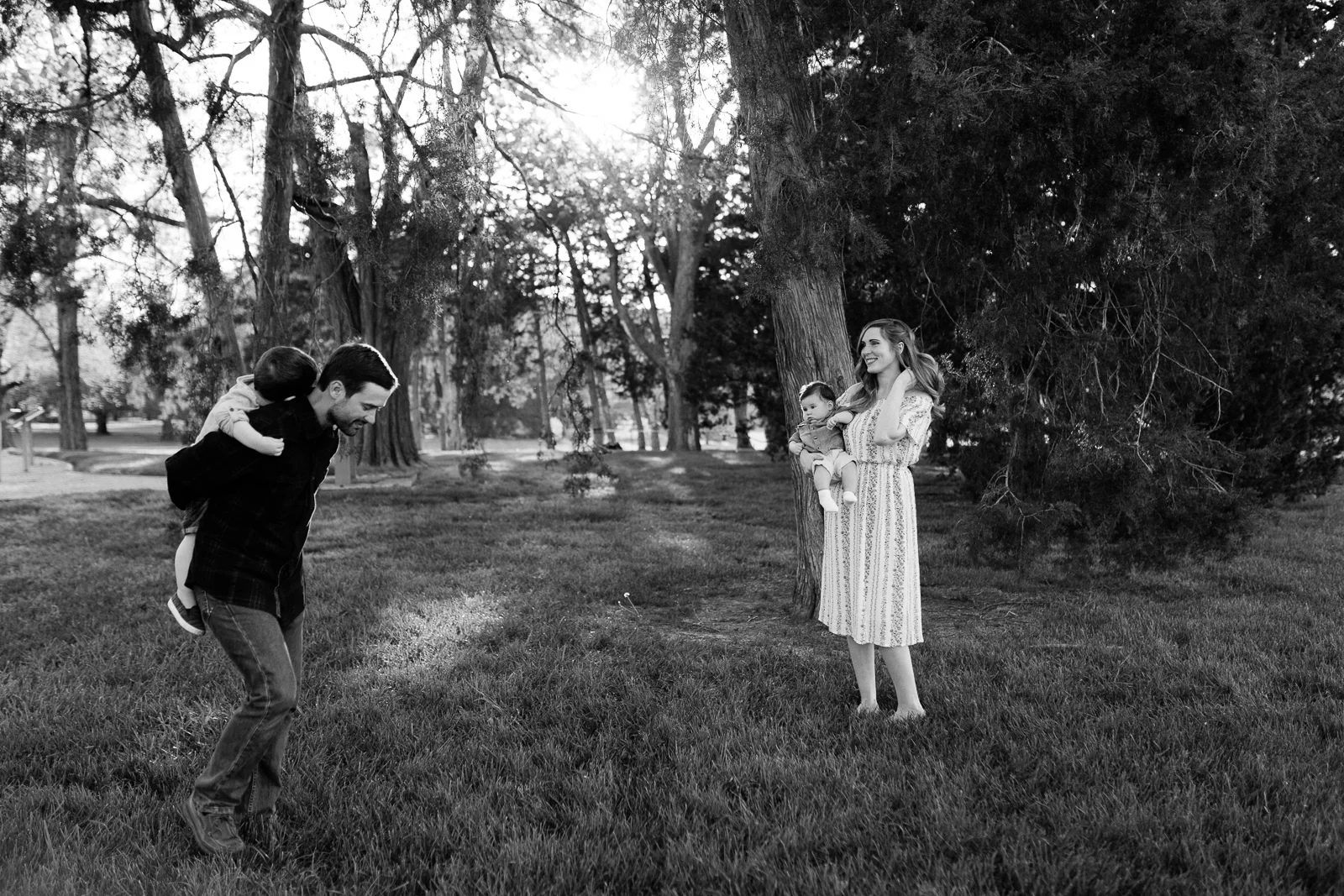 Father gives his son a piggyback ride in the park while mother watches, real life family photo, Kansas City lifestyle photographer, Rebecca Clair Photography