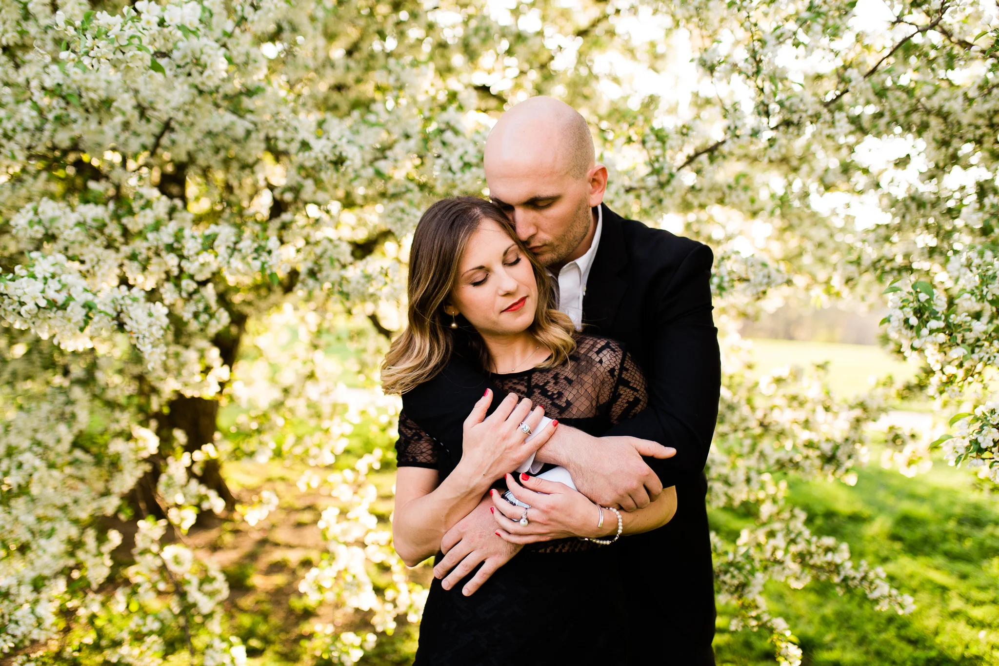 Couple embraces in the golden evening light, apple blossom engagement session at Loose Park, Kansas City natural light photographer, Rebecca Clair Photography