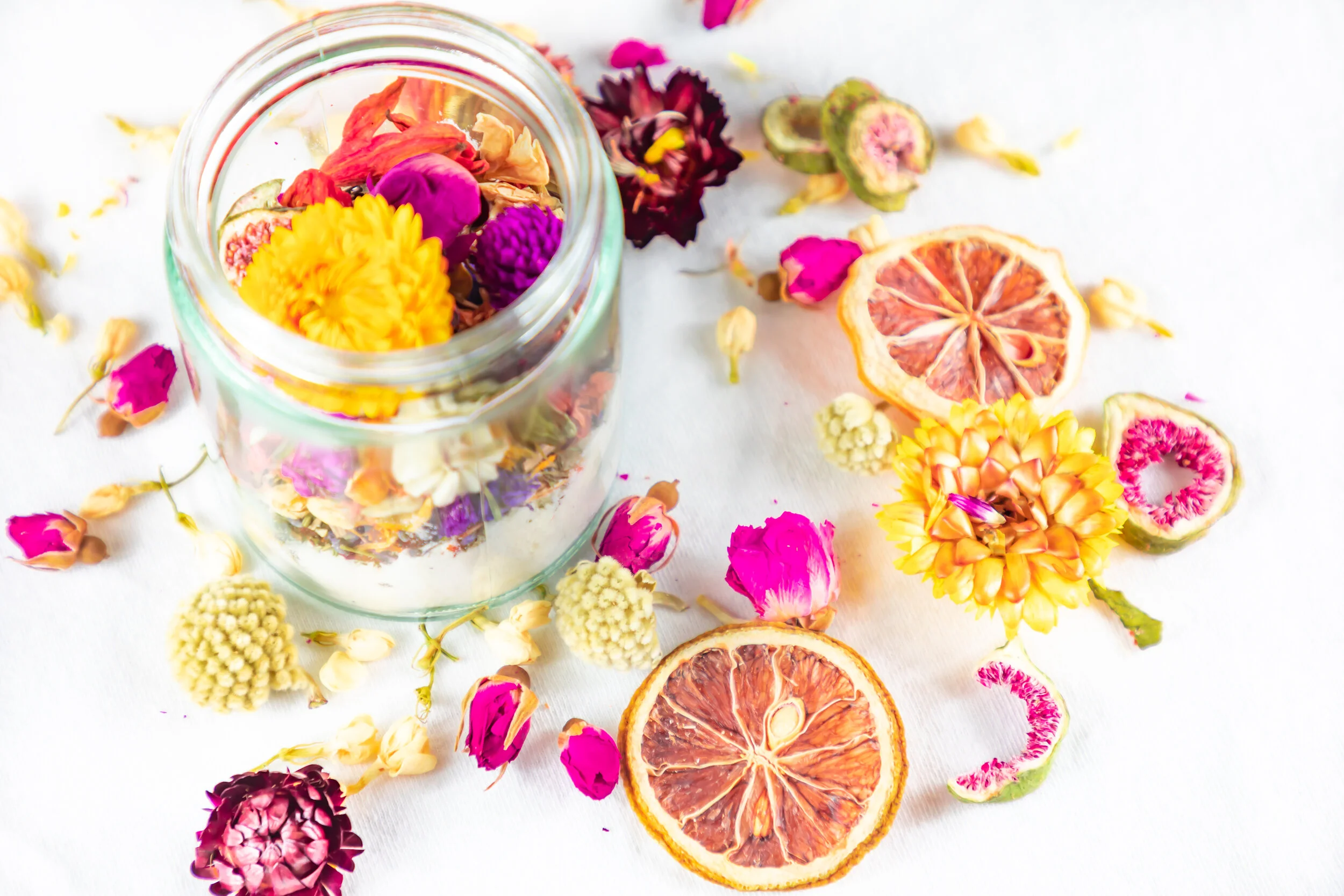 Photo of an open jar containing Milk & Flower bath salts surrounded by many dried fruits & flowers