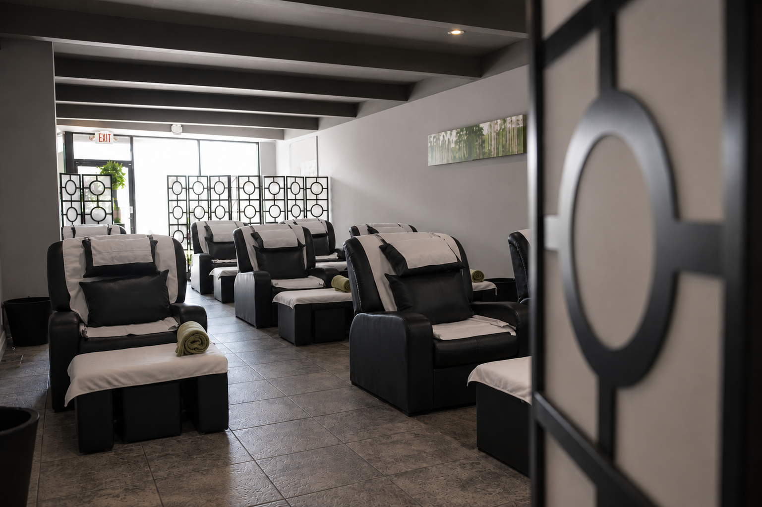 Spa or massage chairs with black and white upholstery and rolled towels, arranged in rows inside a modern wellness center or salon.